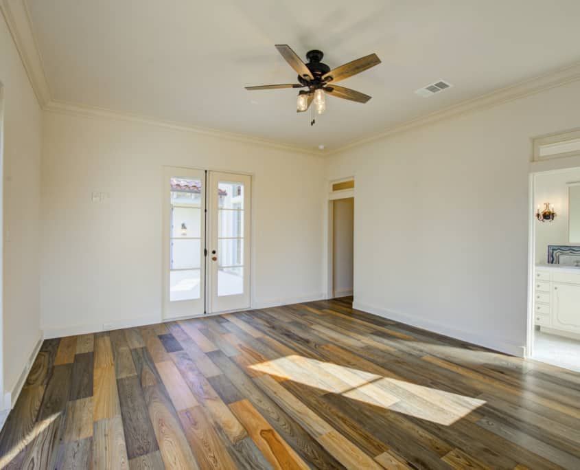 Empty room with wood floor, double doors, ceiling fan, and access to a bathroom.