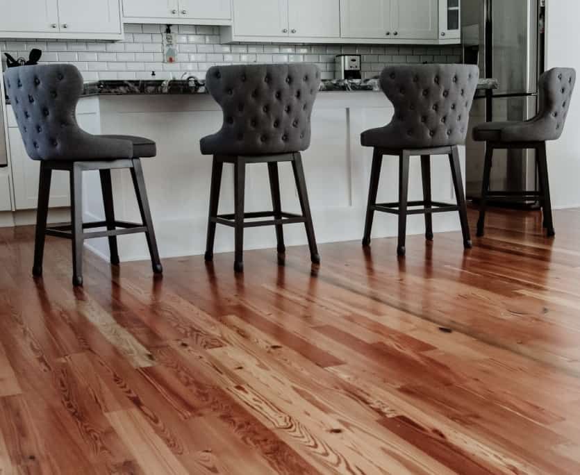 Four gray upholstered bar stools at a kitchen island, hardwood floor.
