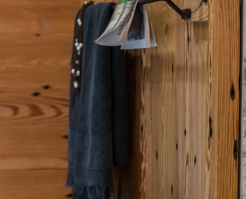 Dark towel, necklace, and papers hanging from a black metal bar on wooden wall.