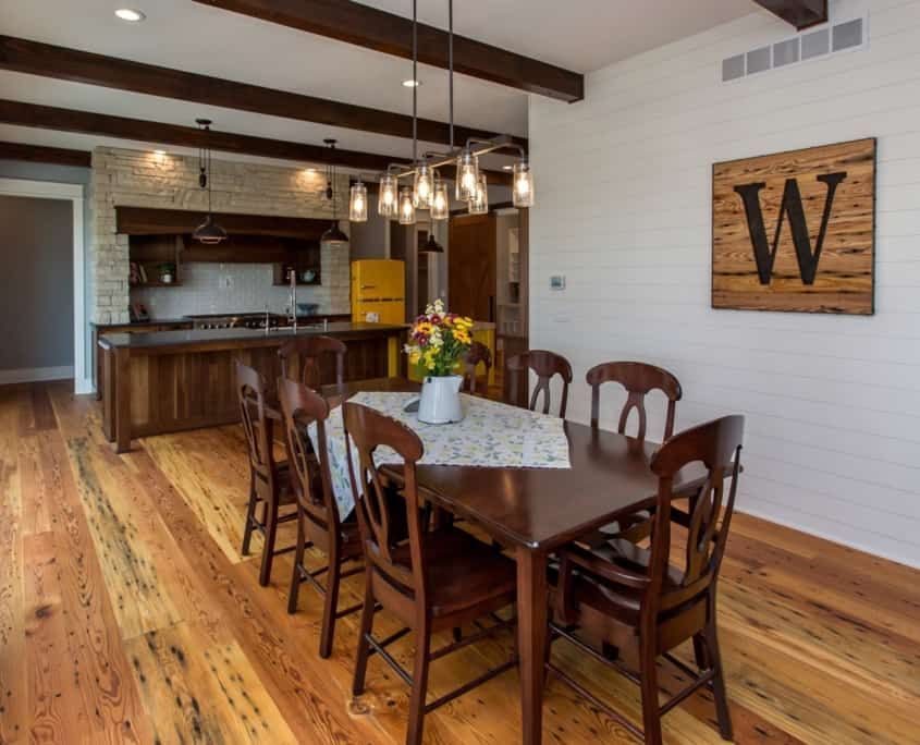 Dining room with wood table and chairs, kitchen in background. Yellow refrigerator. Wood floors and ceiling beams.
