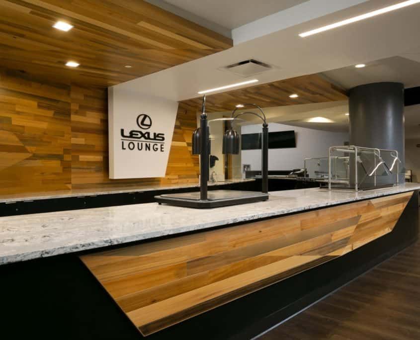 Lexus Lounge interior with a wooden accent wall, countertop bar, and the Lexus logo.