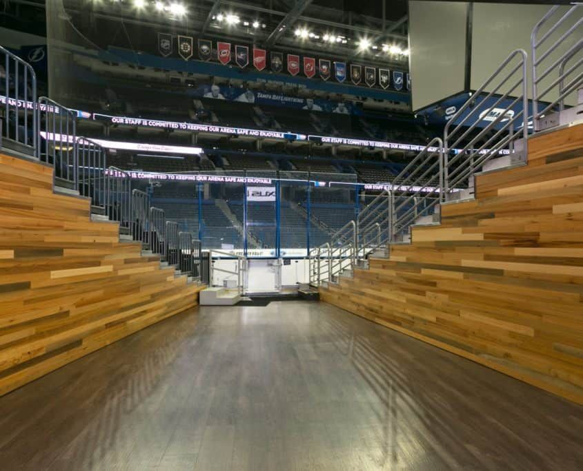 Empty hockey arena, wooden bleachers on both sides, metal railings, looking towards the ice.