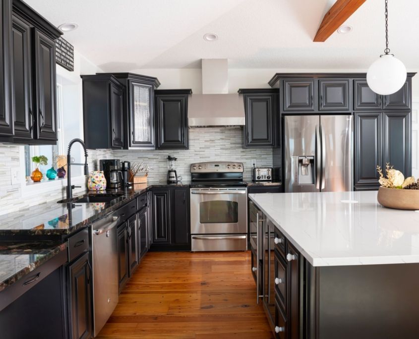 Dark kitchen with black cabinets, stainless steel appliances, and a white countertop island.