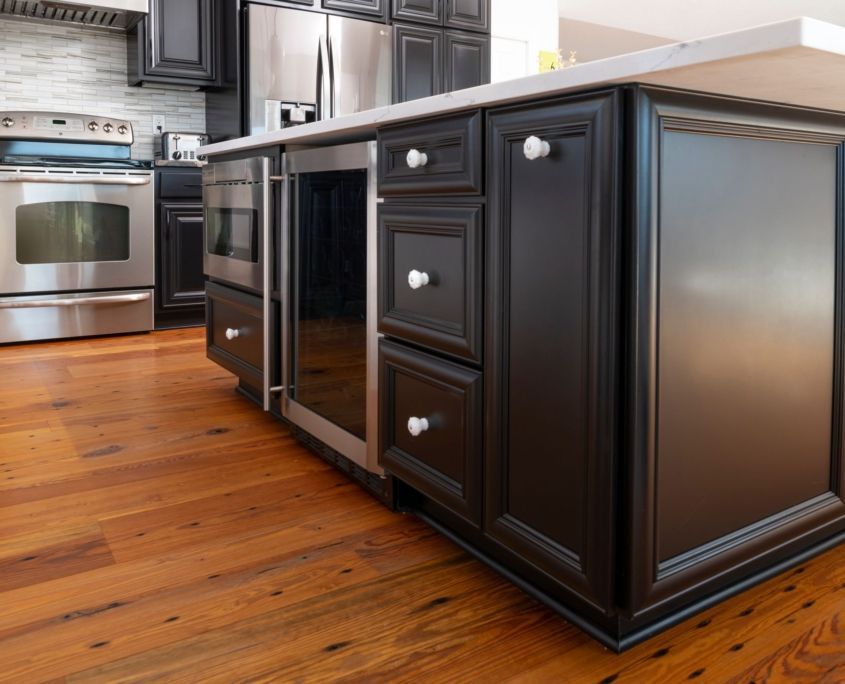 Dark kitchen island with a wine fridge, cabinets, and hardwood floors.
