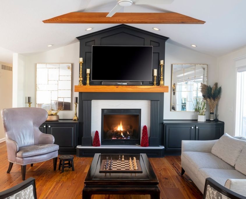 Living room with fireplace, TV, and seating; black mantel, hardwood floors, and white walls.