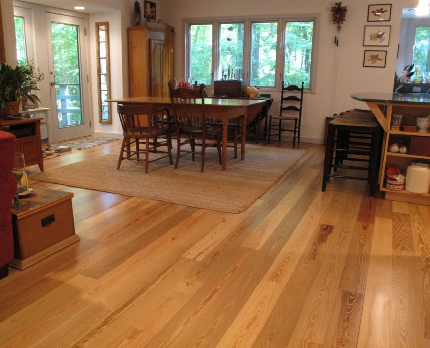 Hardwood floor in a dining room with a wooden table, chairs, and natural light from large windows.