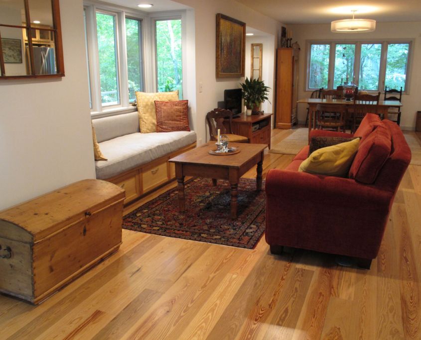 Living room with hardwood floors, sofa, bay window seat, wooden chest, and dining area.