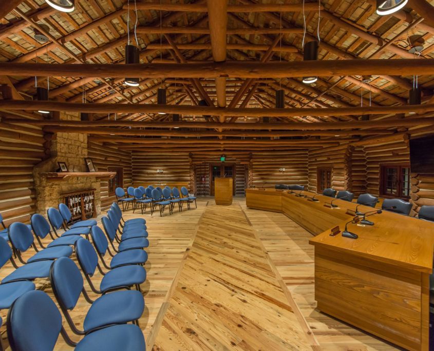 Interior of a log cabin meeting room with blue chairs, wooden tables, and a podium.