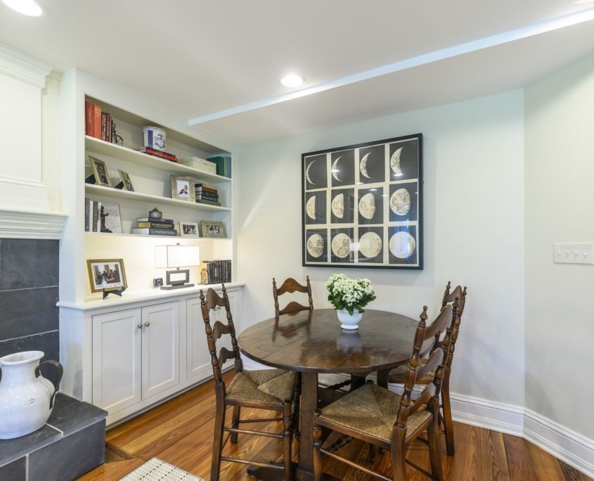 Dining nook with round table, four chairs, built-in shelves, framed art, and fireplace.
