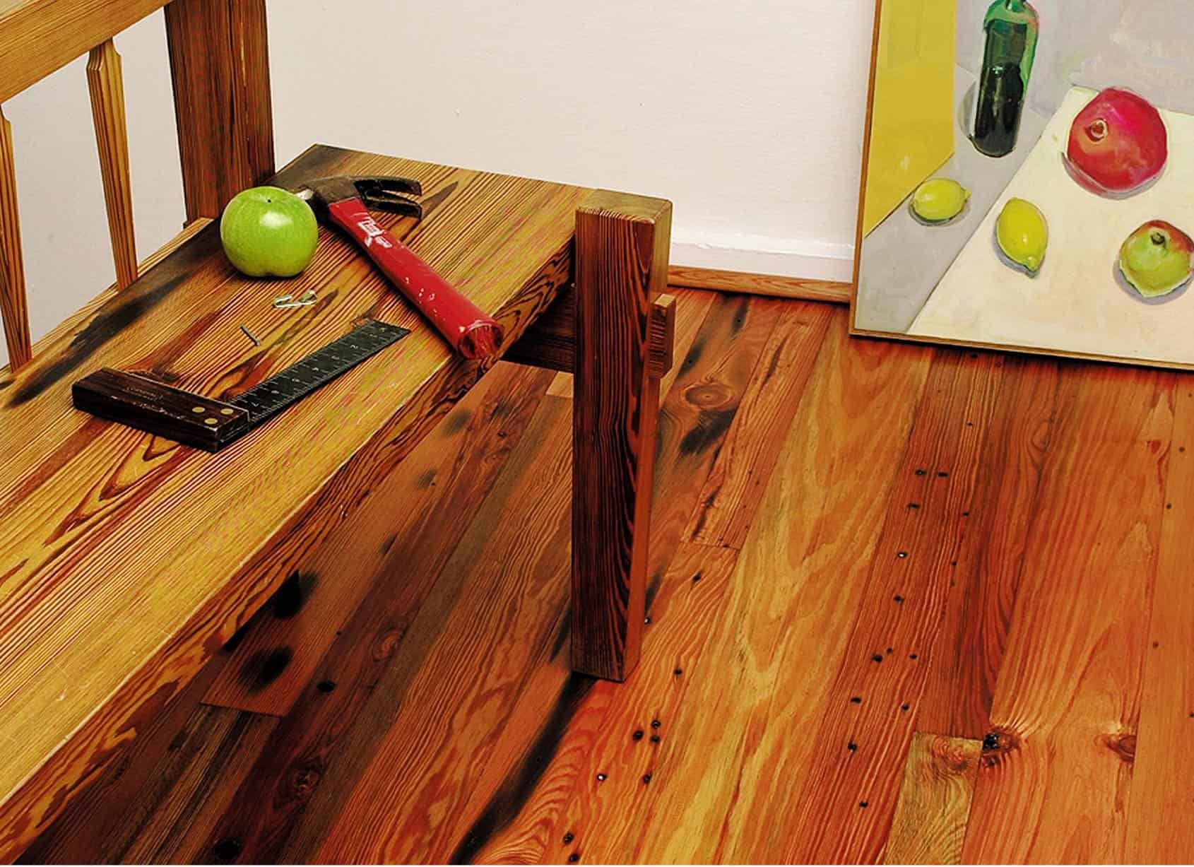 Wooden bench with tools and an apple. Painting of fruit nearby on wooden floor.