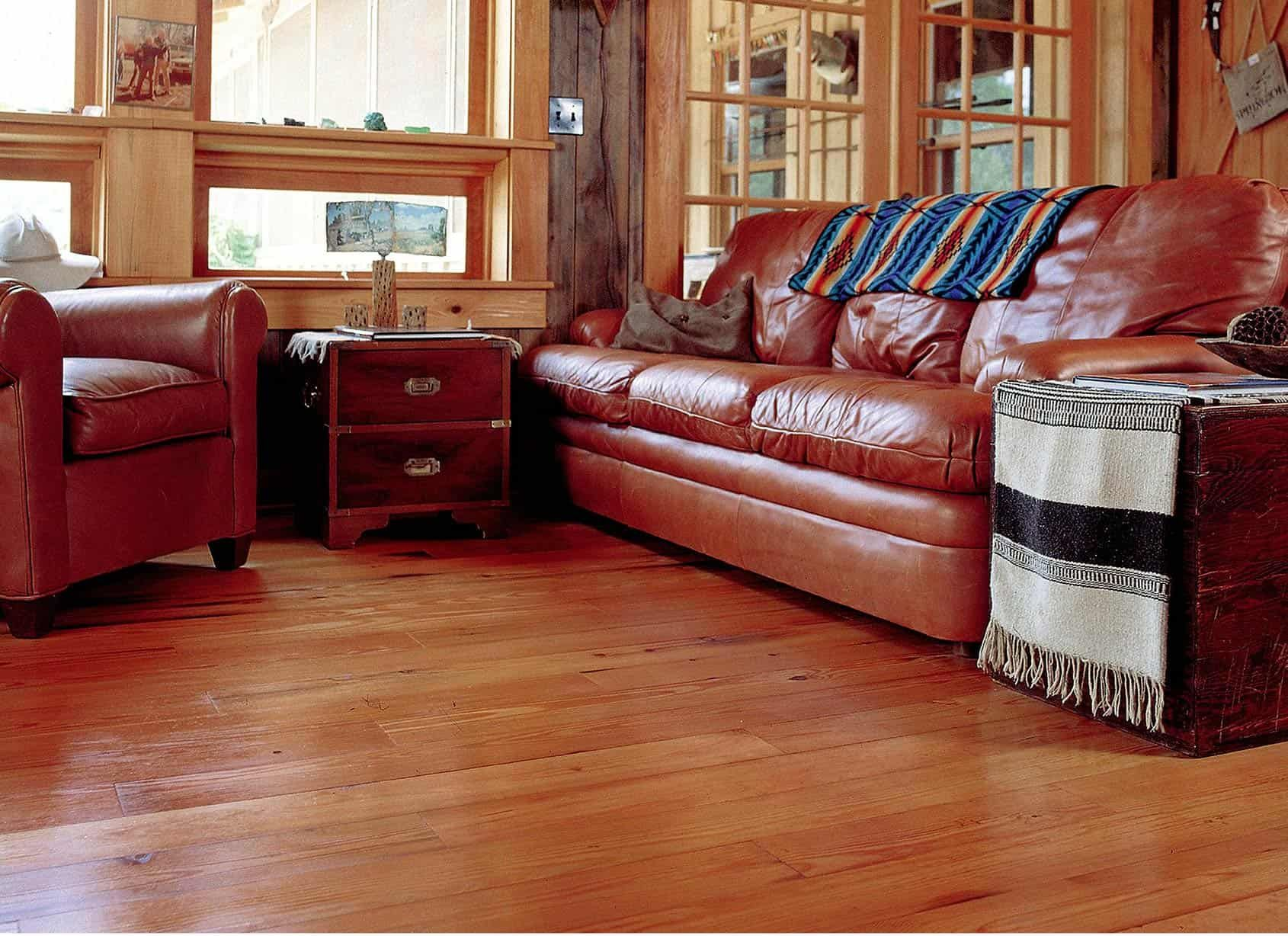 Living room with brown leather sofa, armchair, wood floors, and side tables.