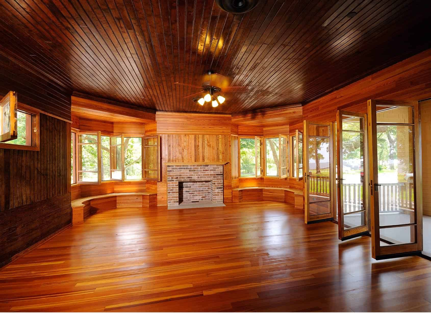 Wooden-paneled interior room with hardwood floors, bay windows, fireplace, and open french doors leading to a porch.
