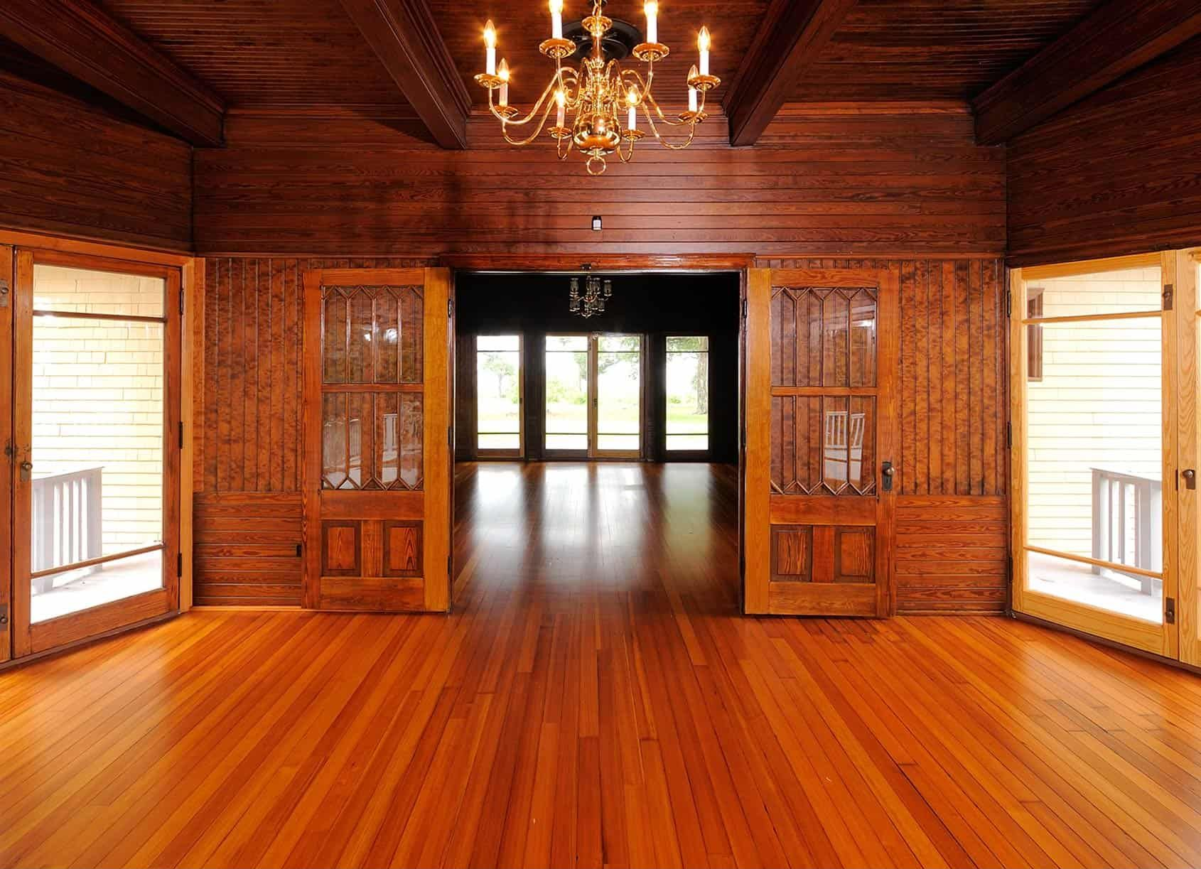 A wood-paneled room with open doors leading to a bright outdoor space; a chandelier hangs from the ceiling.