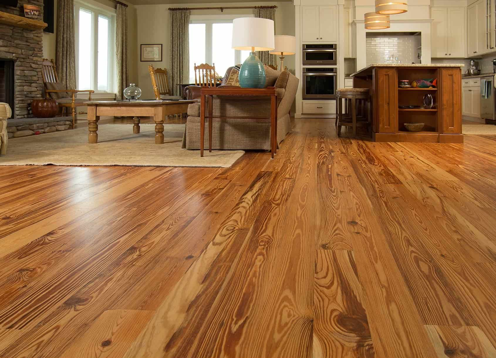 Hardwood floor in a living room with furniture, fireplace, and kitchen in the background.