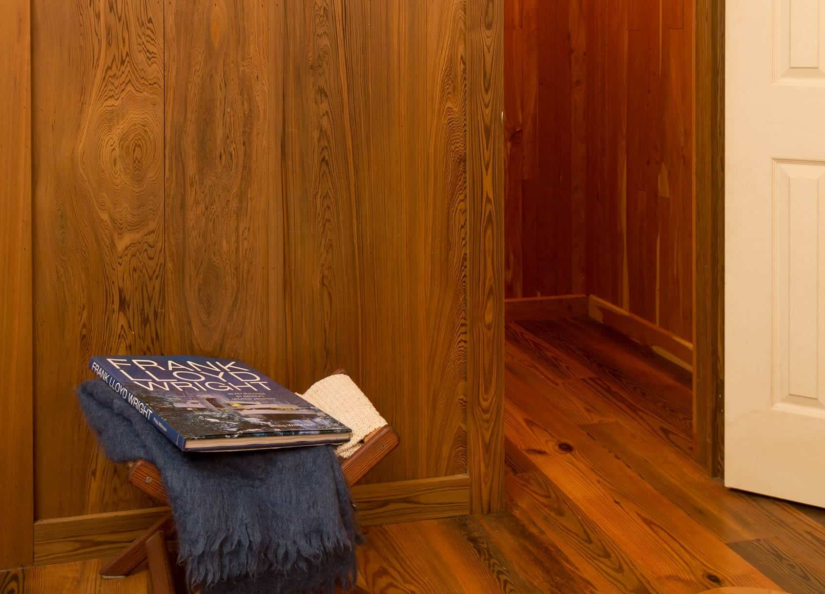 Wooden paneled room with book on a stool and doorway to another room.