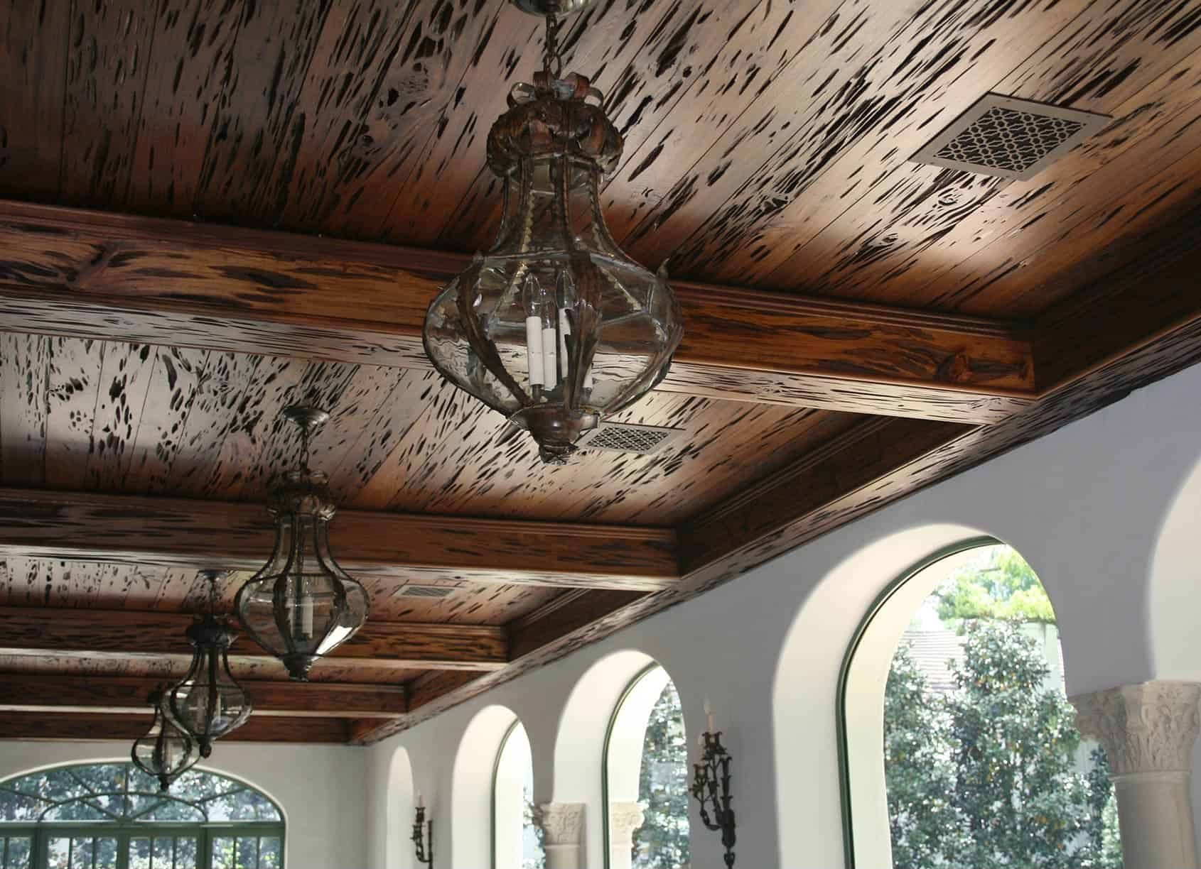 Ornate chandeliers hang from a wood-paneled ceiling with dark accents, arched windows along a white wall.