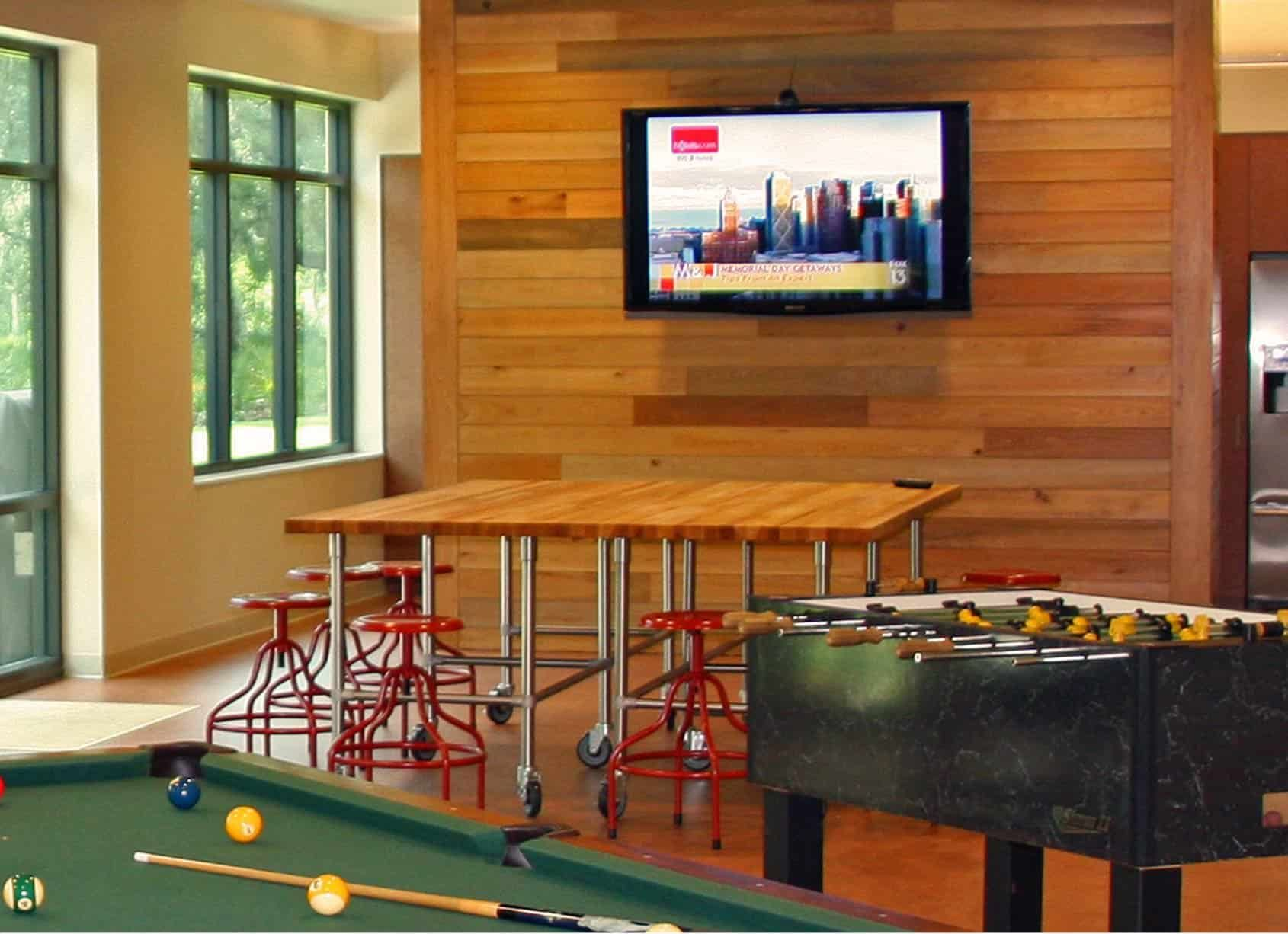 Game room with pool table, foosball, high table with stools, and TV on wood panel wall.