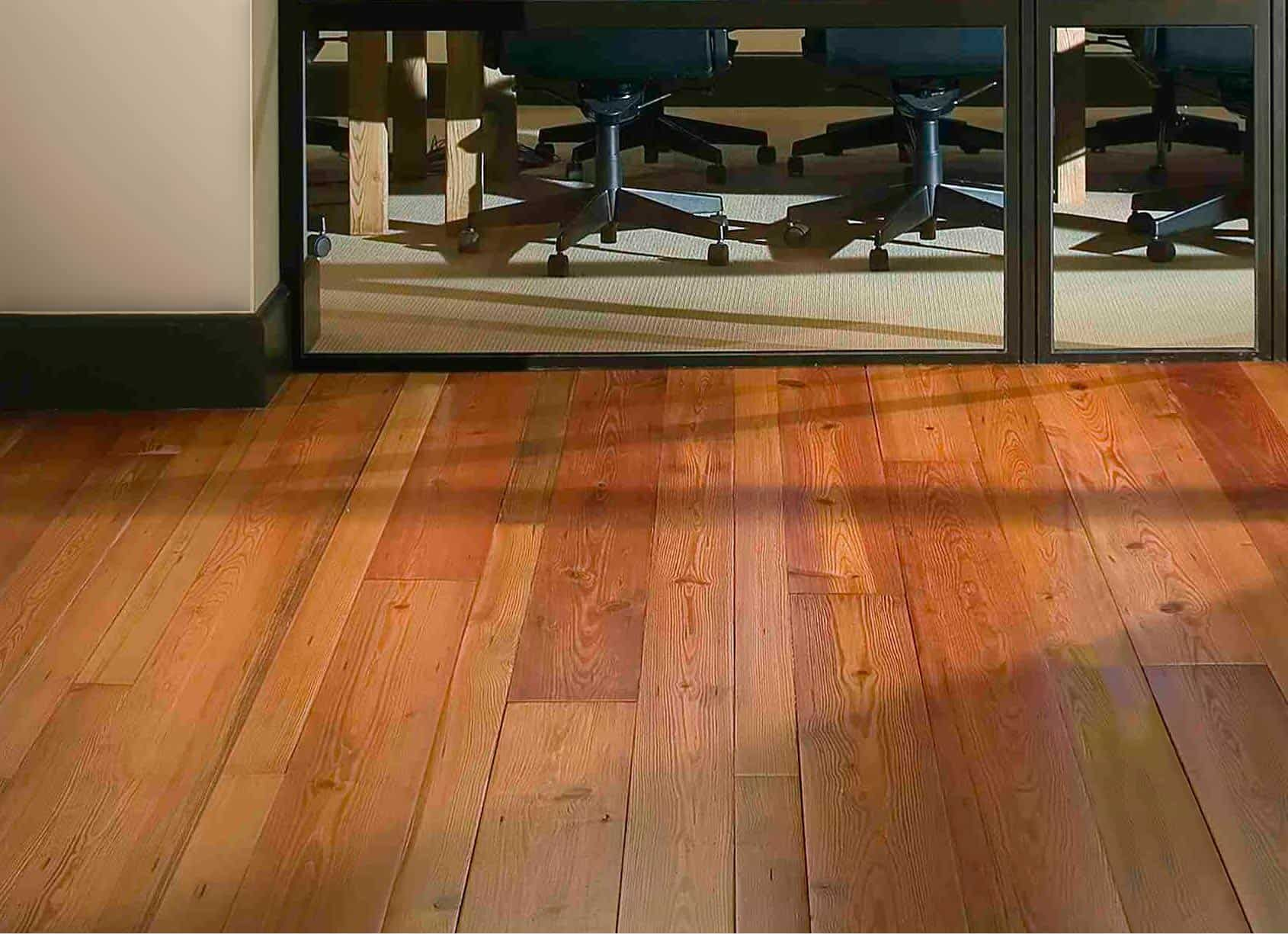 Hardwood floor in front of a metal framed barrier, with office chairs visible beyond it.
