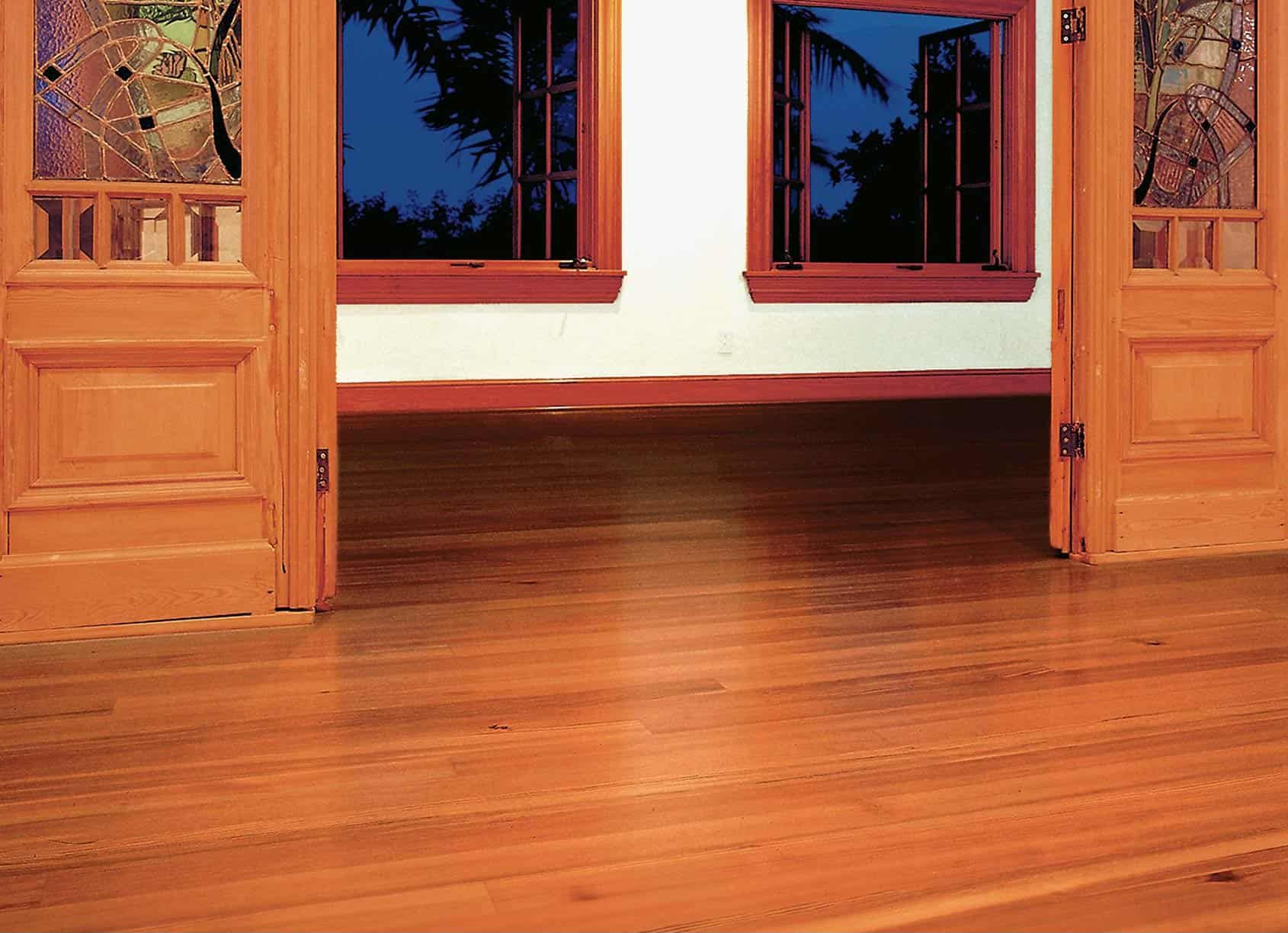 Wooden doors open to a room with hardwood floors, two windows, and white walls.