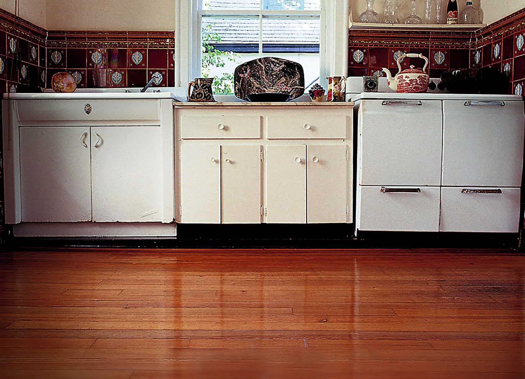 Kitchen with wooden floor, white cabinets, tiled backsplash, and window with outdoor view.