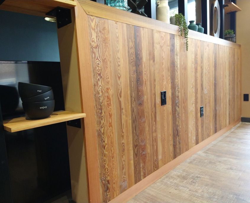 Wooden panel wall with vertical planks, featuring a shelf and electrical outlets.