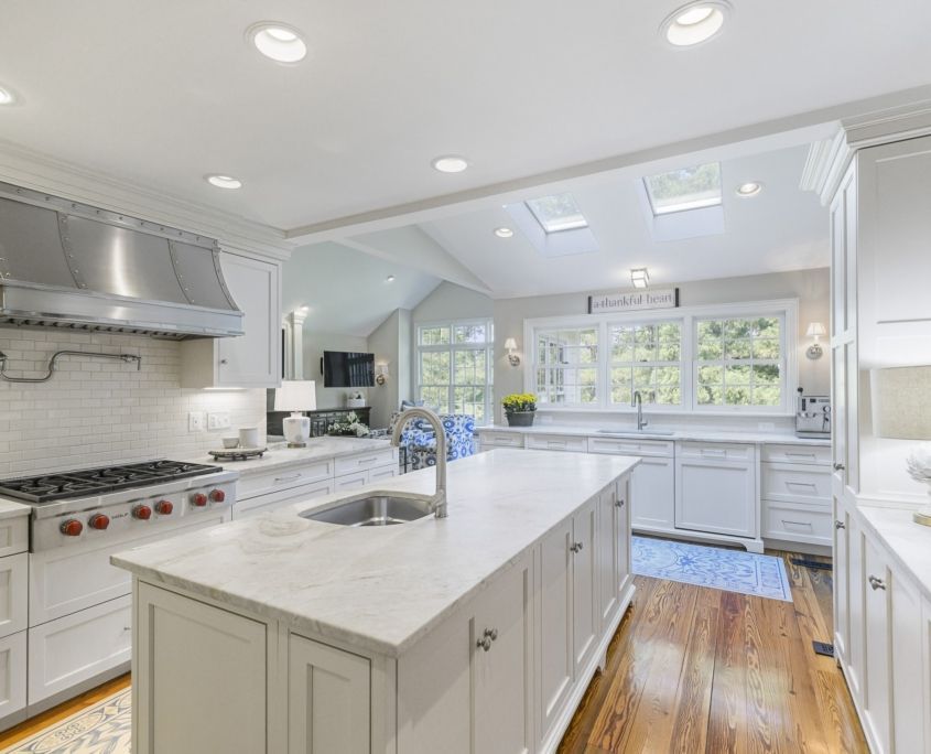 White kitchen with island, stainless steel range hood, skylights, and hardwood floors.