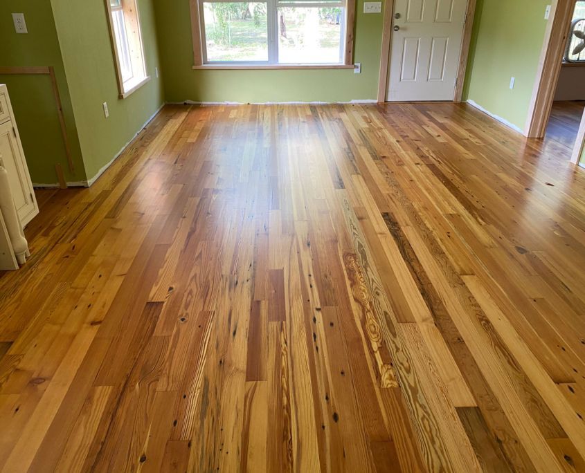 Hardwood floor with natural wood grain, in a room with green walls, a window, and a white door.