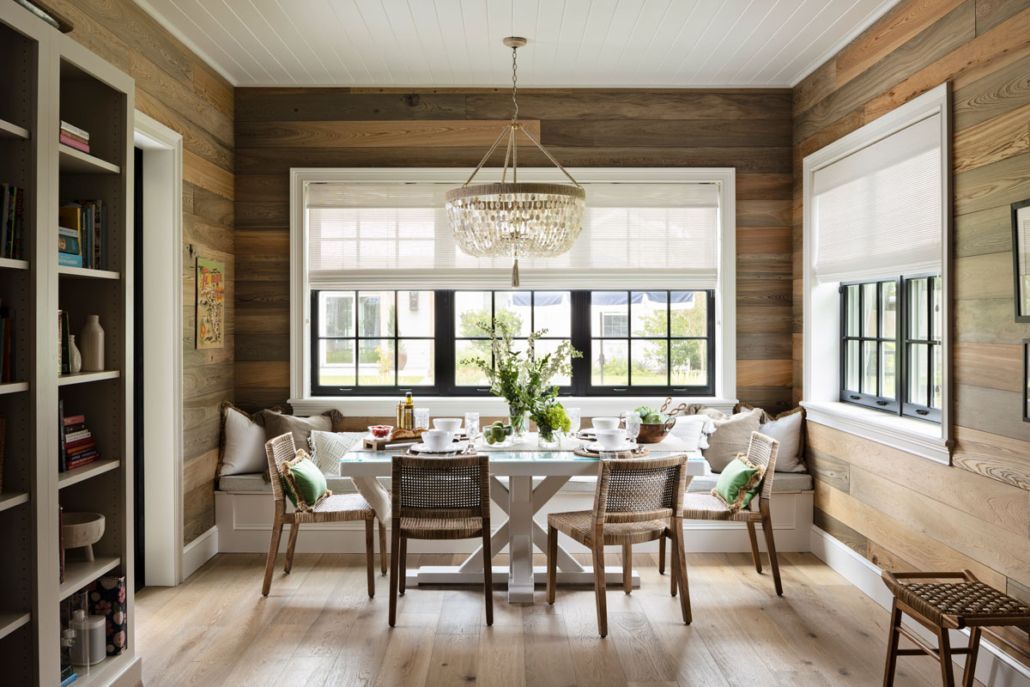 Dining room with wooden walls, white table and chairs, large windows, and a chandelier.
