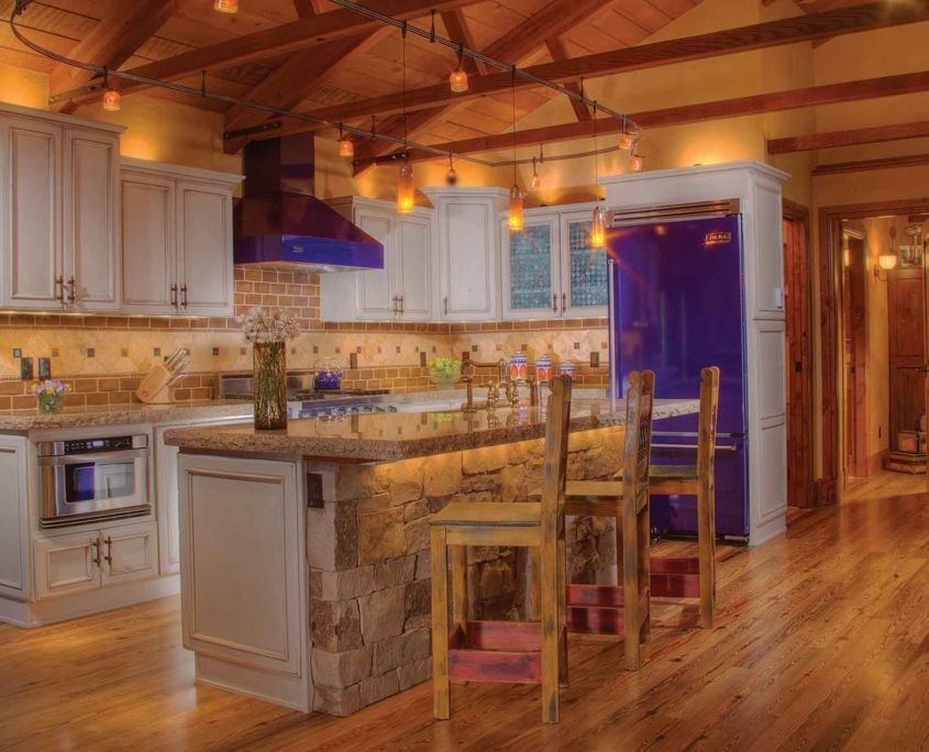 Kitchen with light wood ceiling, white cabinets, stone island, blue appliances.