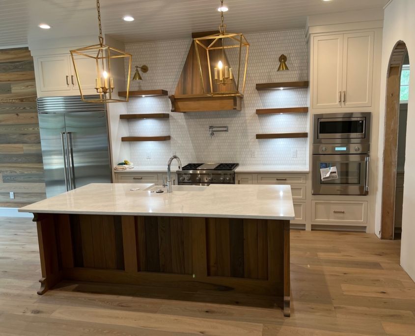 Kitchen with island, light wood floor, white cabinets, gold pendant lights, and wooden range hood.