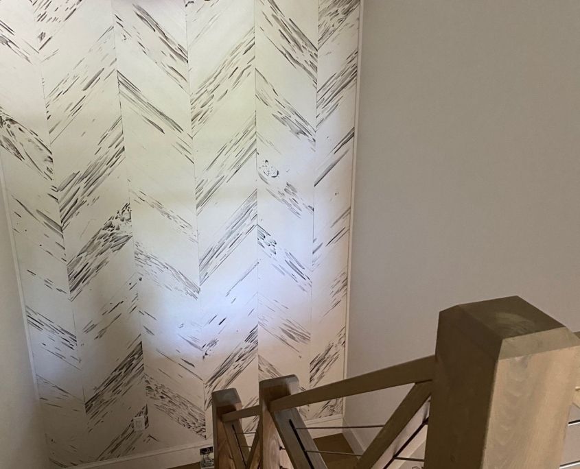 Staircase with wooden railing and chevron patterned wallpaper in white and gray.