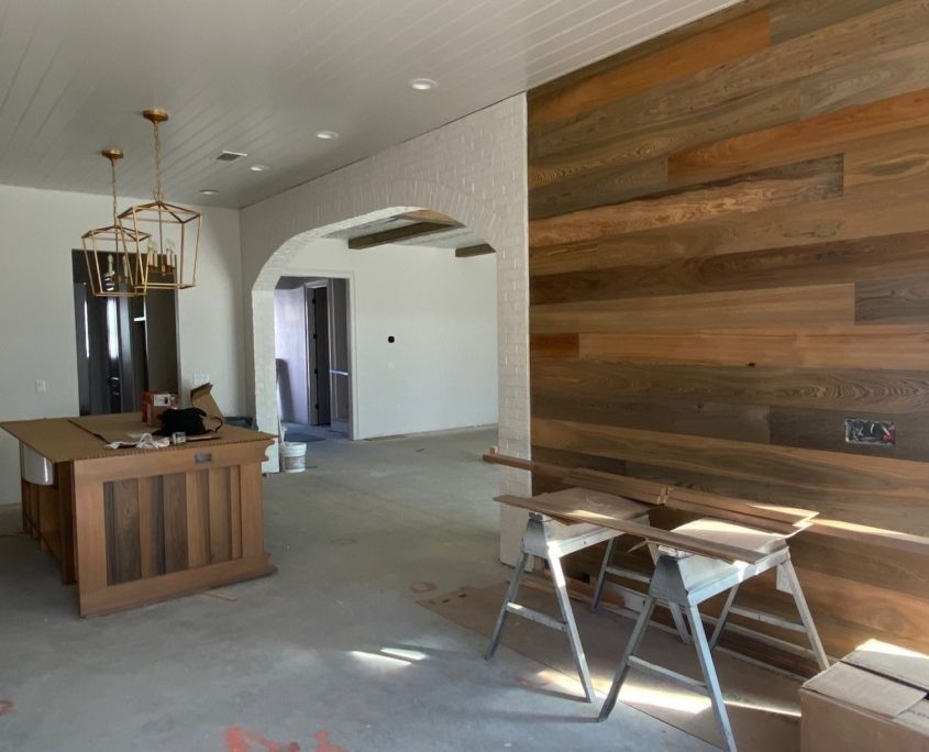 Interior with wood accent wall, kitchen island, gold light fixtures, and archway. Construction in progress.