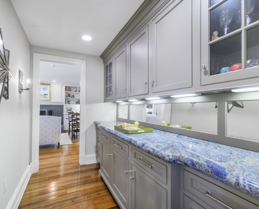 Gray cabinets with blue countertop in a hallway, leading to another room.