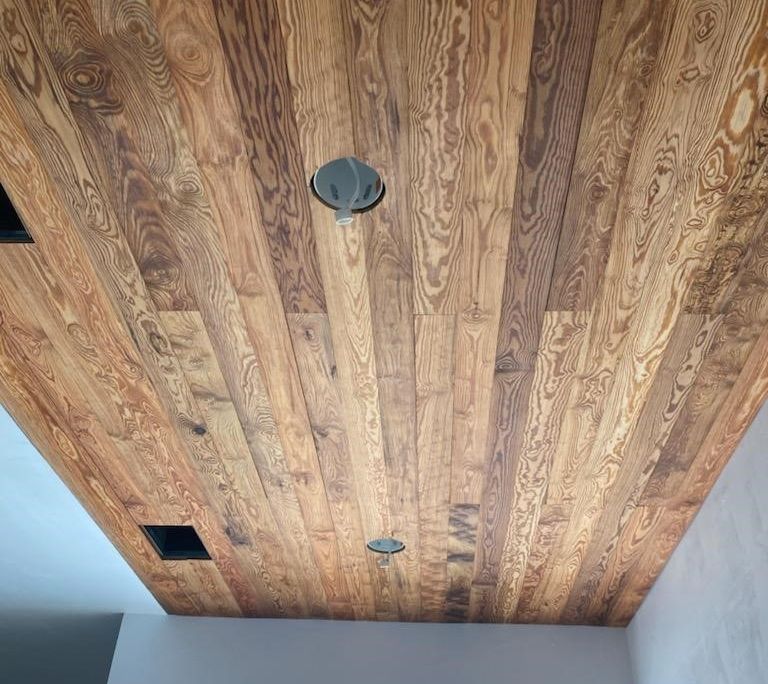 Wooden plank ceiling with recessed lighting and vent openings.