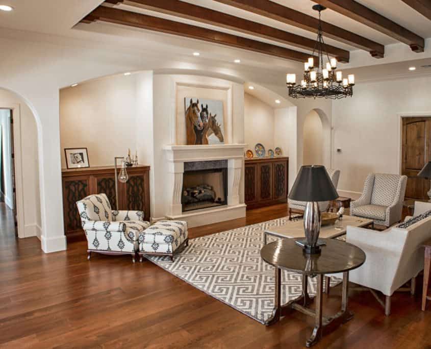 Living room with fireplace, wooden beams, hardwood floor, seating, area rug, and chandelier.