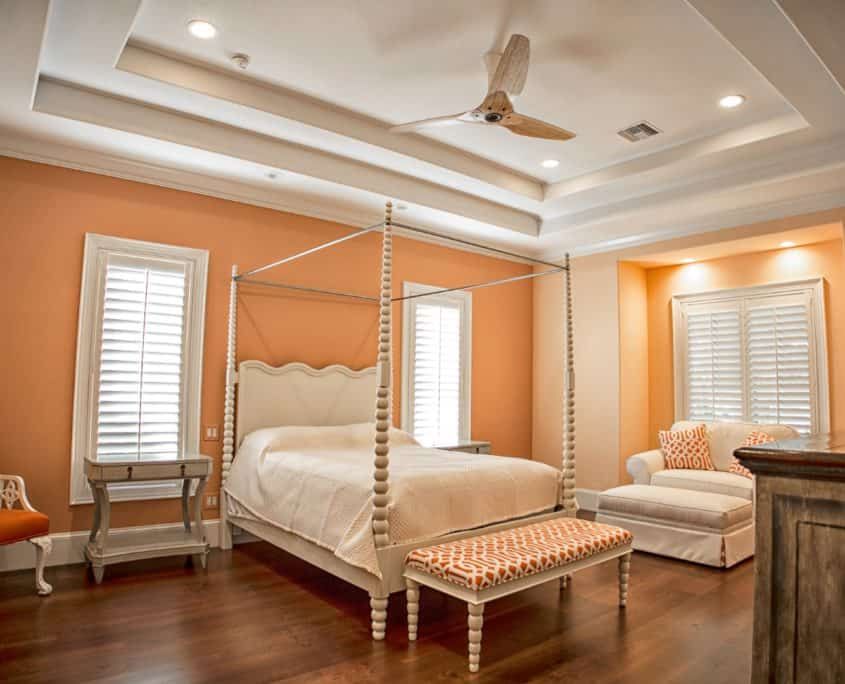 Bedroom with peach walls, white bed, ceiling fan, and wooden floor.
