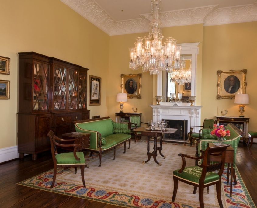 Elegant yellow-walled room with green furniture, fireplace, large chandelier, and dark wood floors.
