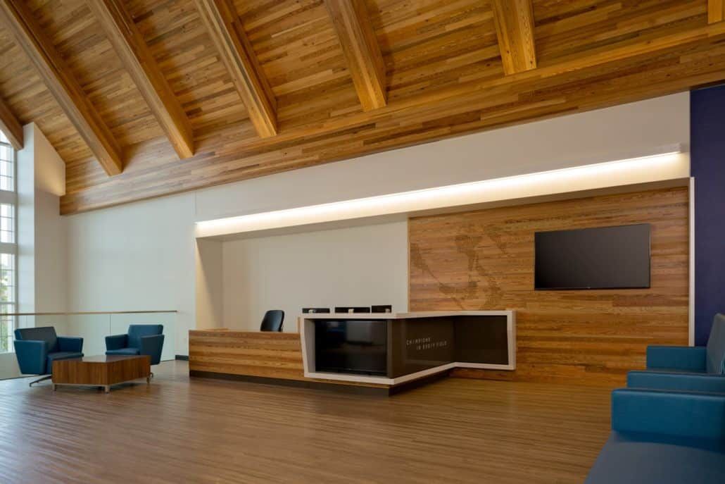 Lobby with wooden floors and ceiling, reception desk, blue seating, and television on a wood-paneled wall.