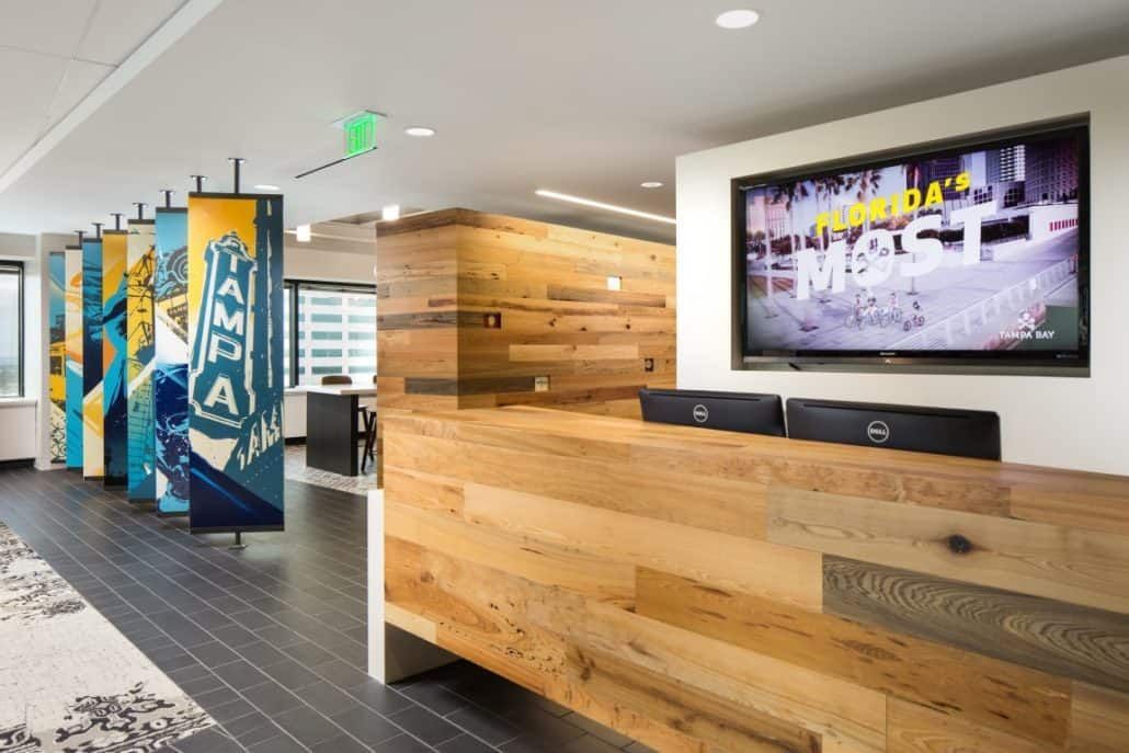 Reception area with wooden reception desk and large TV. Colorful art panels on the left.