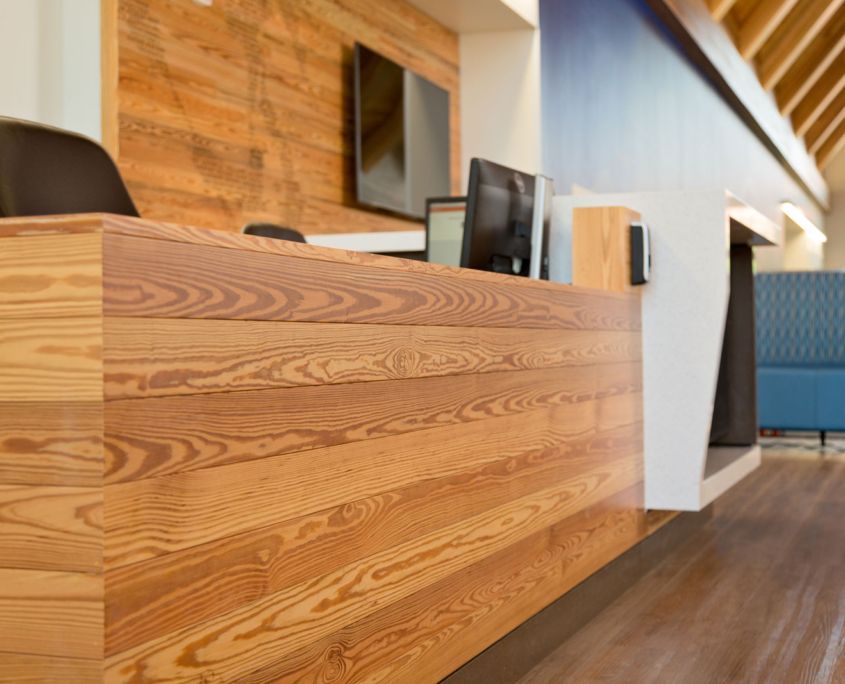 Wooden reception desk in a modern office, with wood paneling and blue wall in the background.