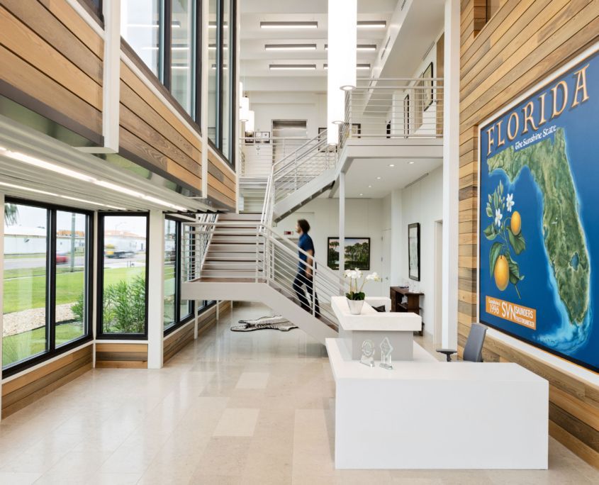 Modern office lobby with staircase, reception desk, and Florida poster.