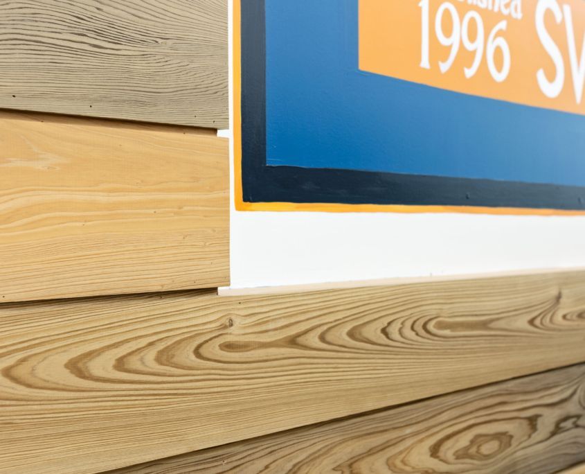 Close-up of wood paneling and a portion of a poster with orange, blue, and white colors.
