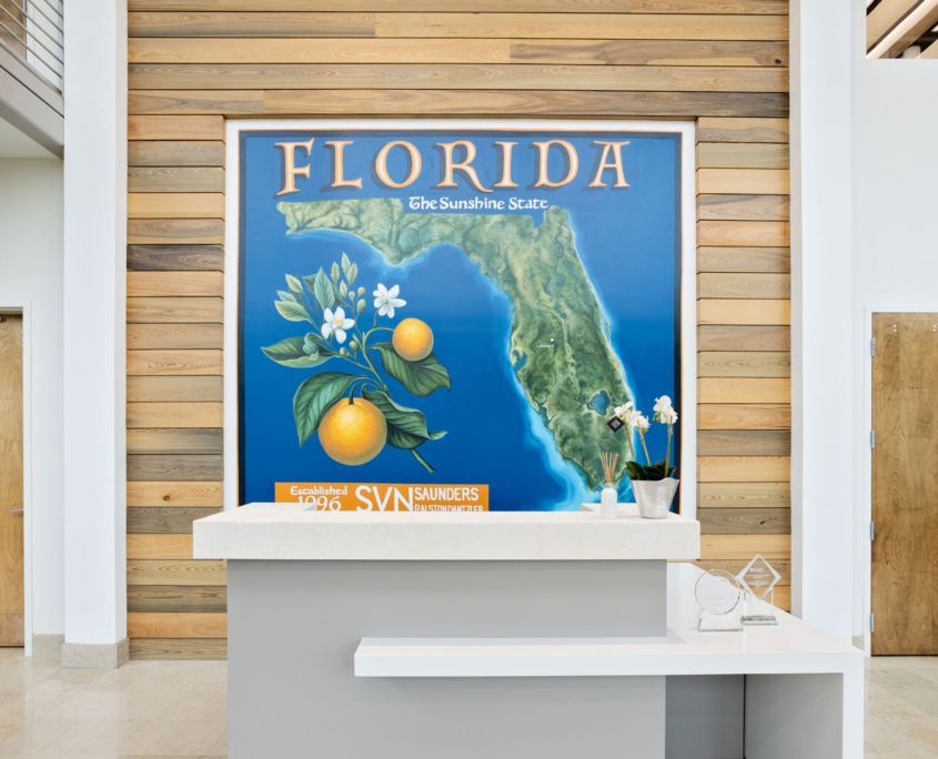 Florida-themed reception area with map art, oranges, and white desk. Wood panel backdrop.