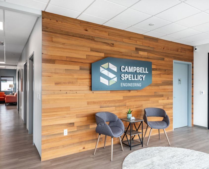 Lobby with Campbell Spellicy Engineering sign on a wood-paneled wall, two gray chairs, a small table, and a circular rug.