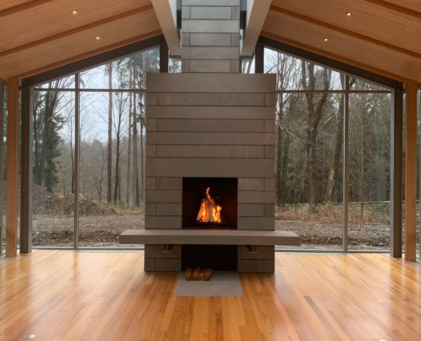 Fireplace in a modern home with large windows and a forest view. Fire is burning.