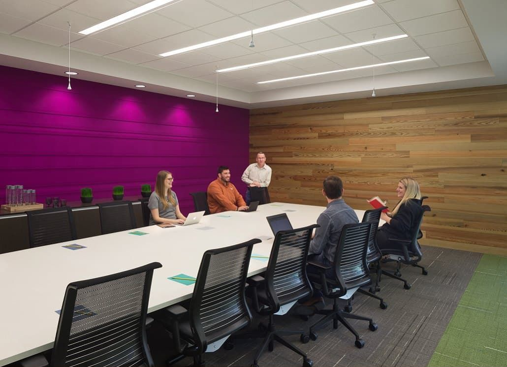 People seated around a long table in a conference room with a purple wall and wooden paneling.