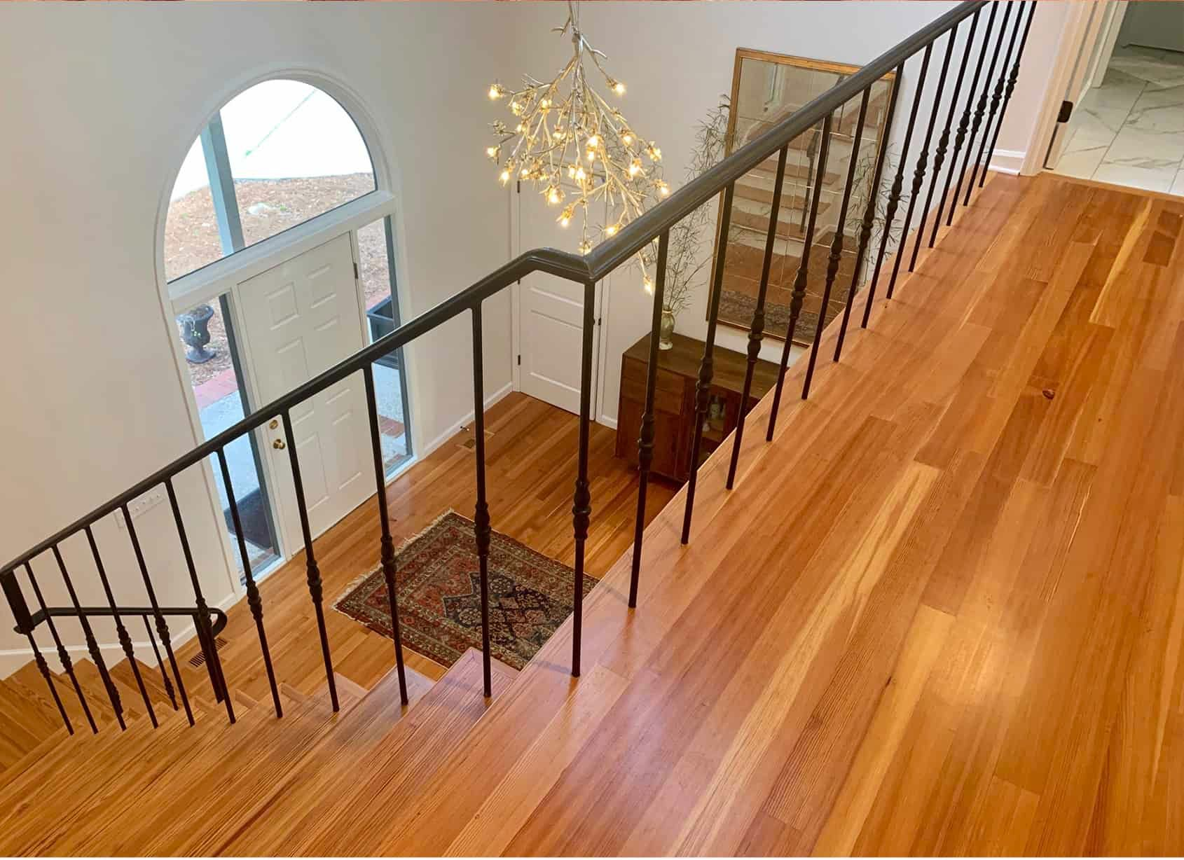 Hardwood staircase with black iron railing, rug, and arched window.