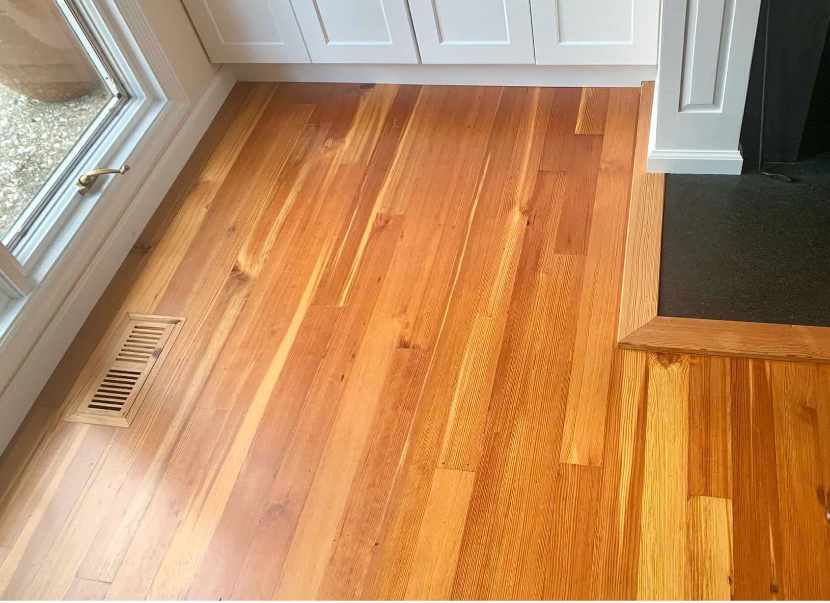 Hardwood floor with a vent next to a window and a black fireplace.