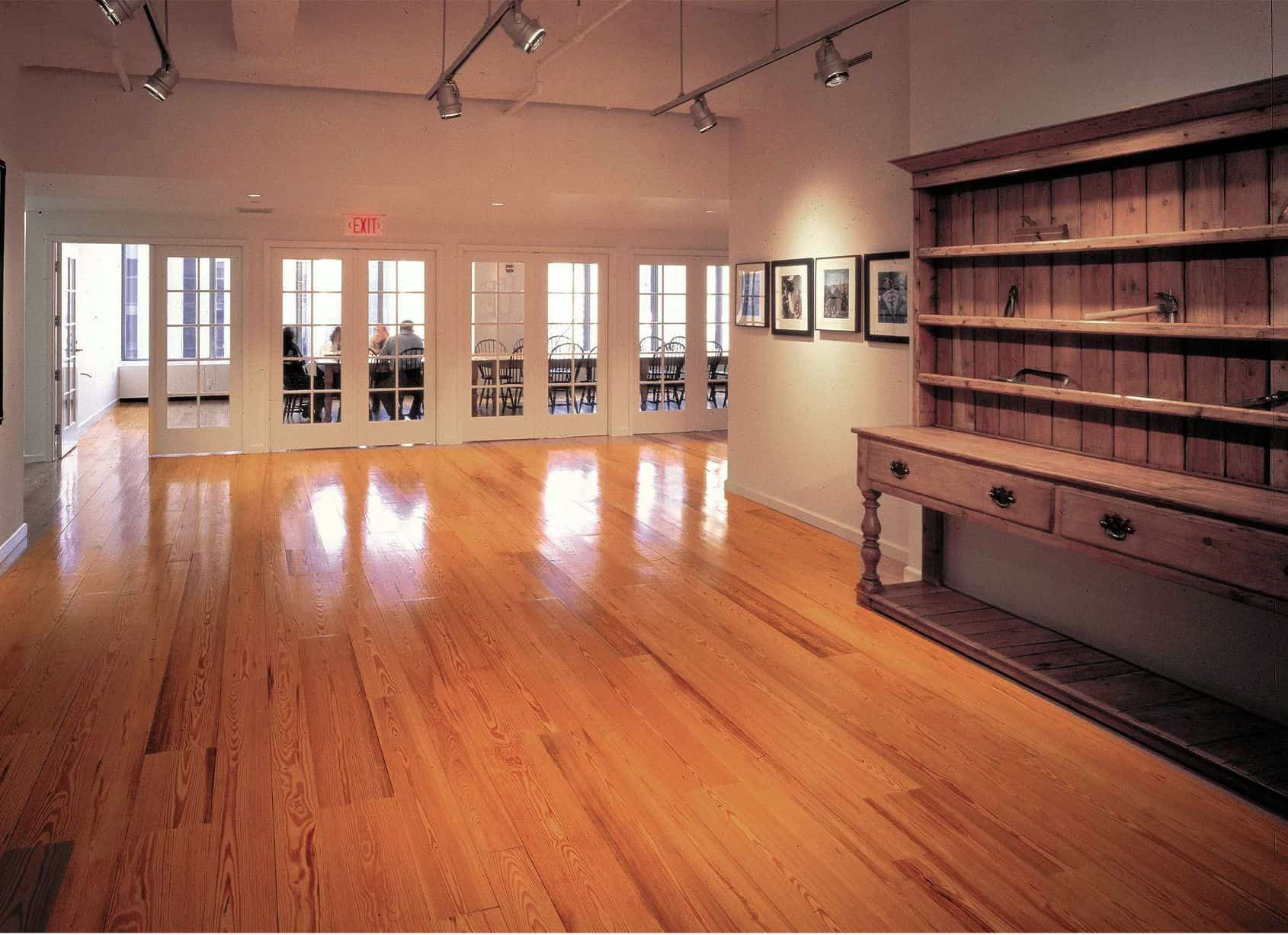 Art gallery interior with polished wood floor, display cabinet, and artwork. People visible through open doors.