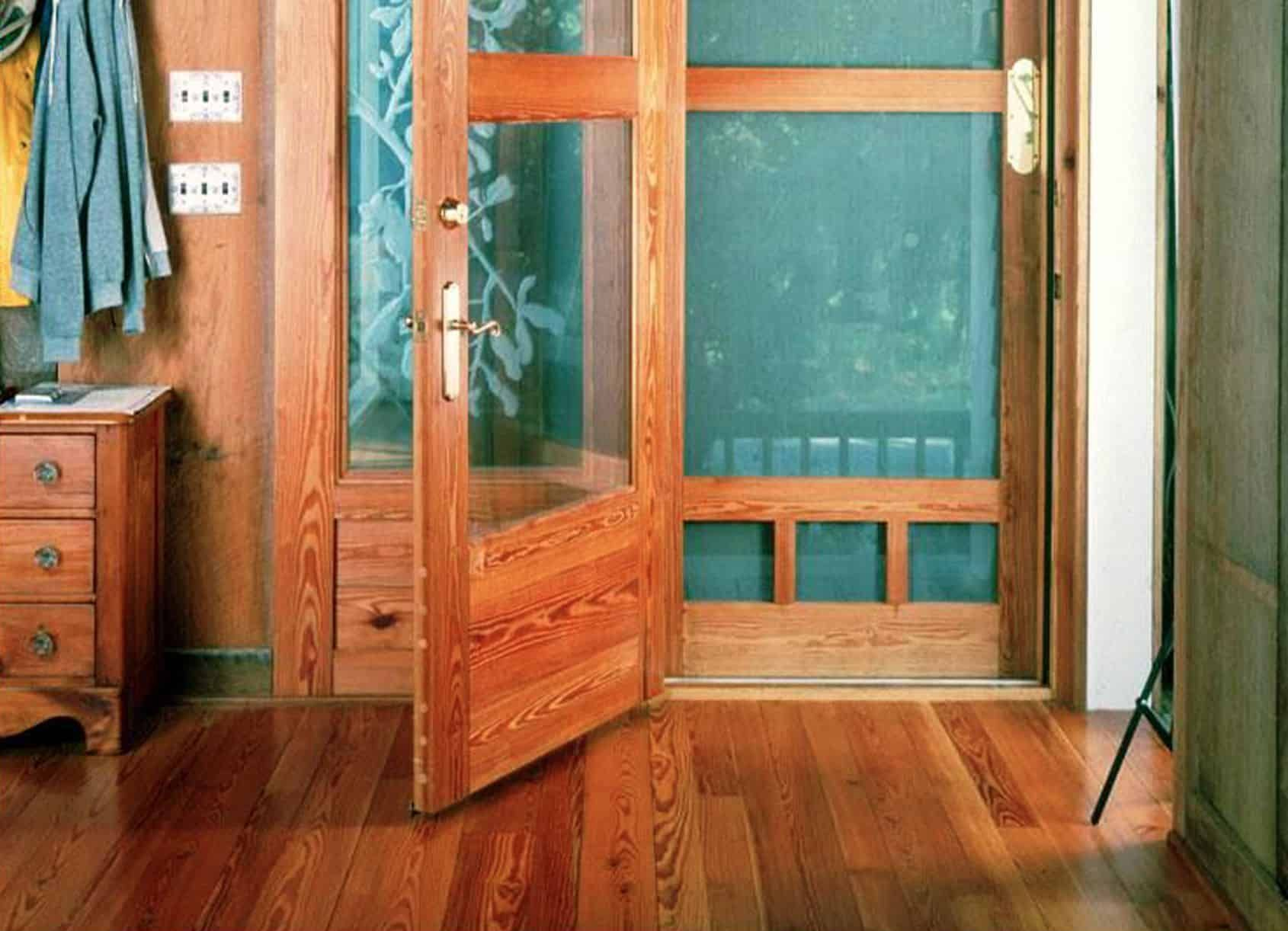 Wooden door open, showing a screen door. Interior wooden floor and paneling.